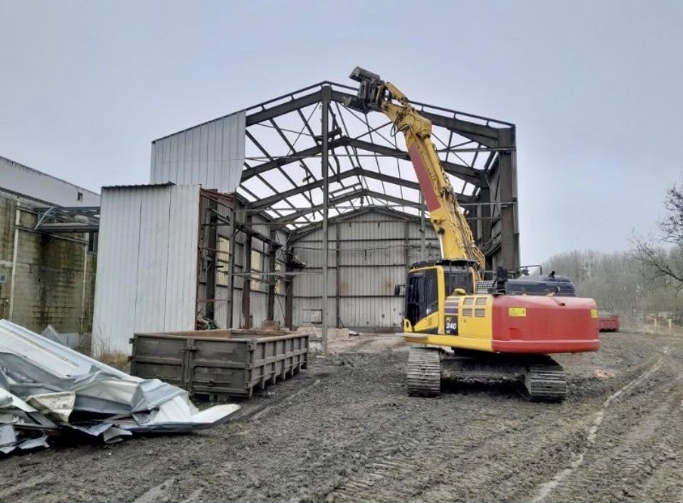 Excavator dismantling a metal-framed hangar.